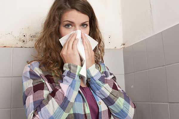 Woman holding a tissue to her knows with mold in the background.